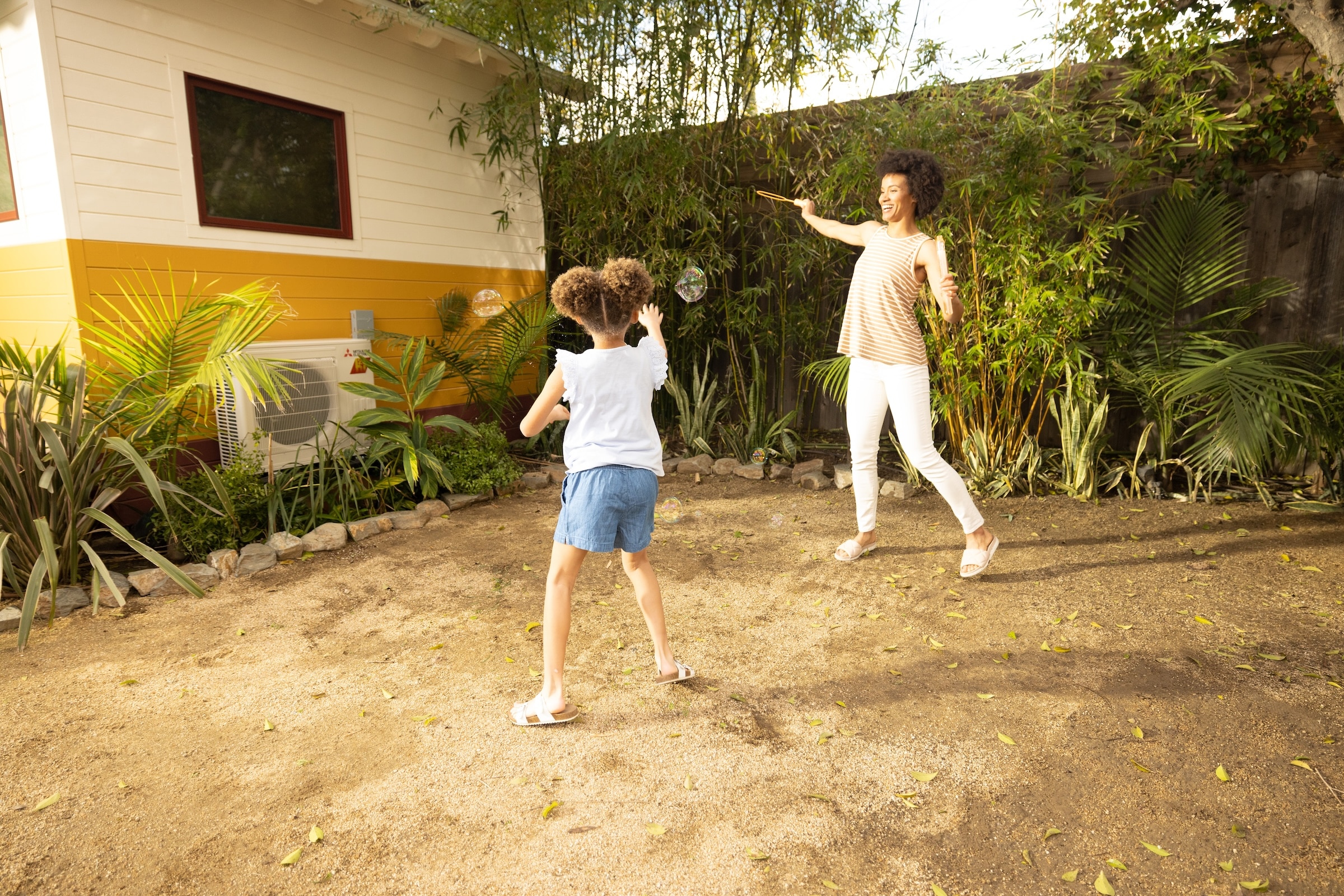 Mother and daughter blowing bubbles in yard with a Mitsubishi heat pump unit outside of the house in the background