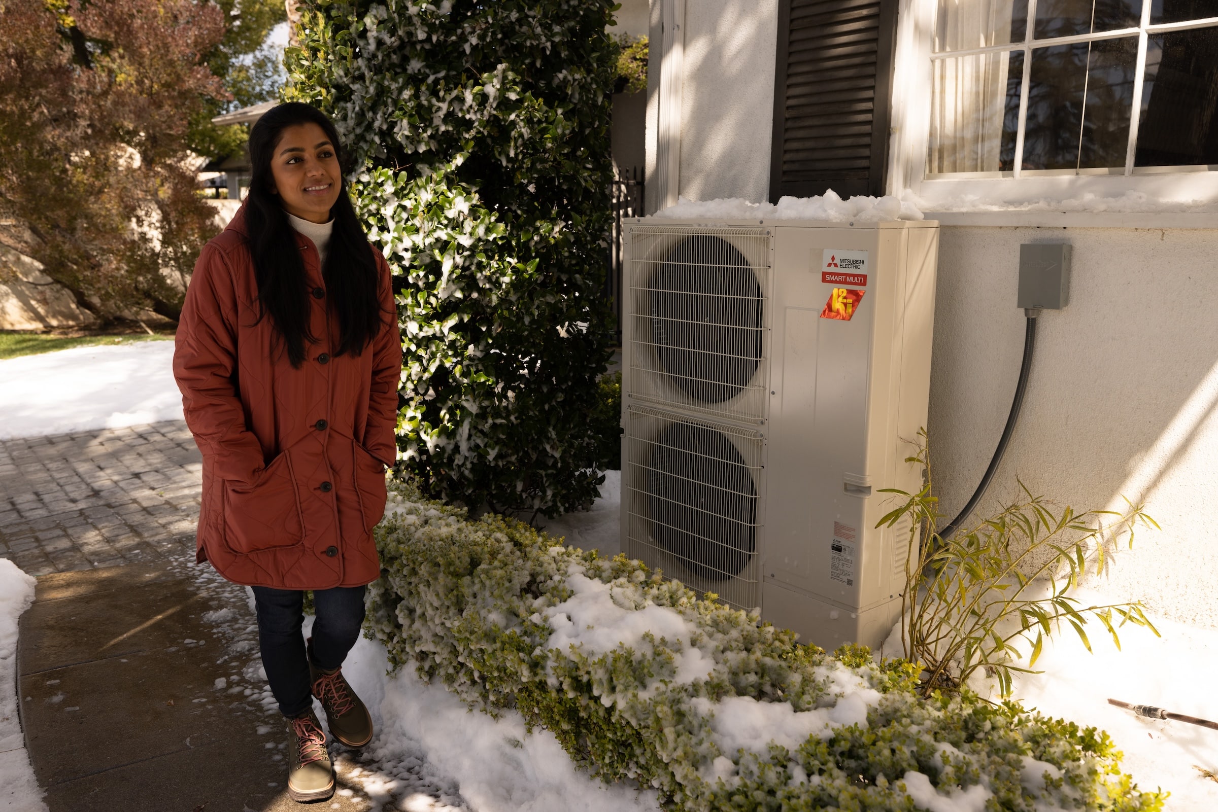Woman standing outside in the snow next to a Mitsubishi heat pump