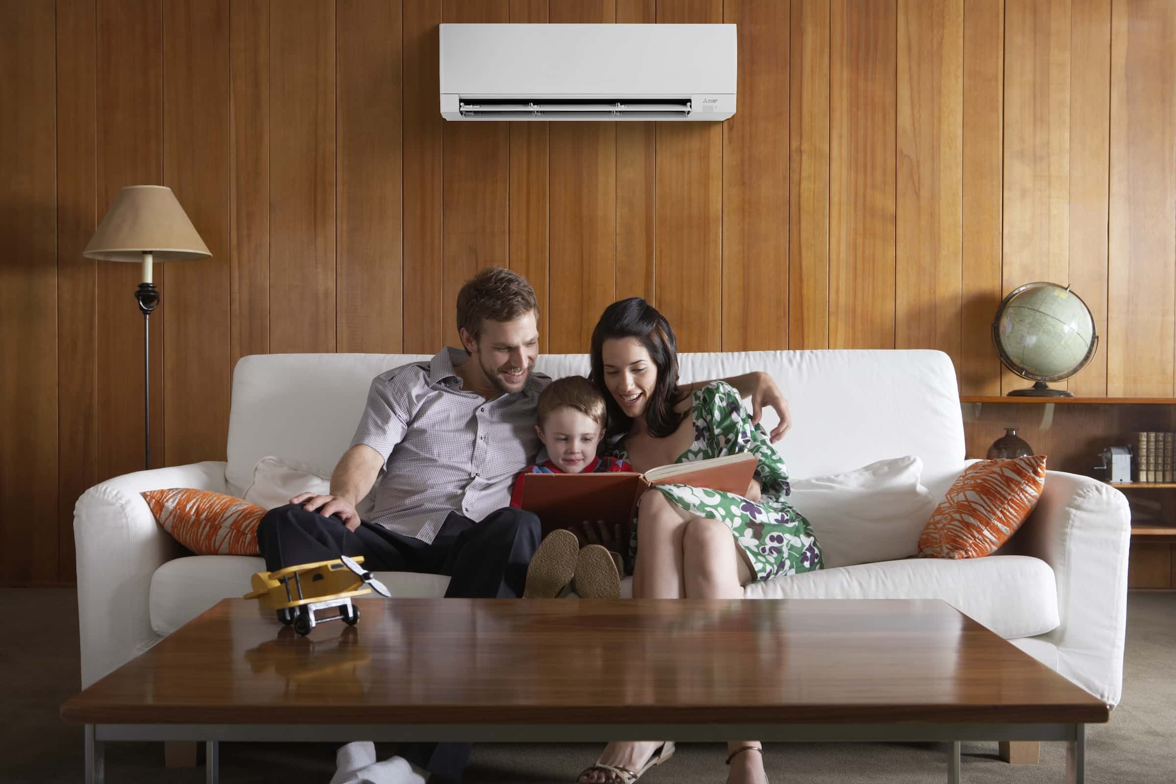 Family reading in living room with a wall-mount Mitsubishi heat pump above them