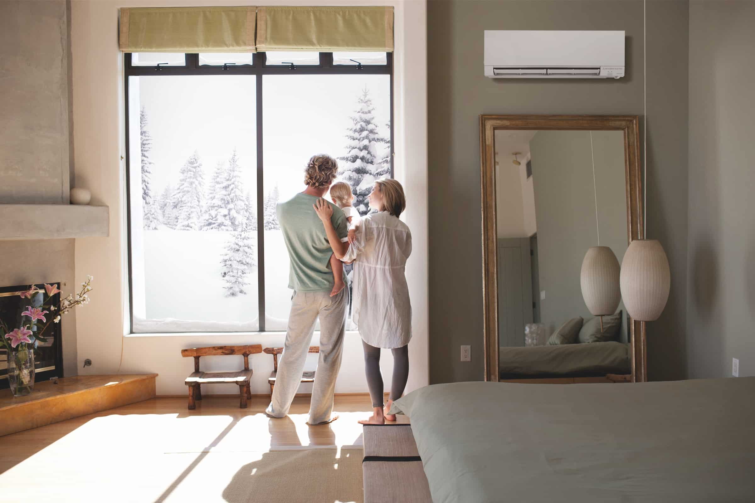 Family standing in living room, looking out the window. A ductless mini-split heat pump register is noticeably on the wall next to them