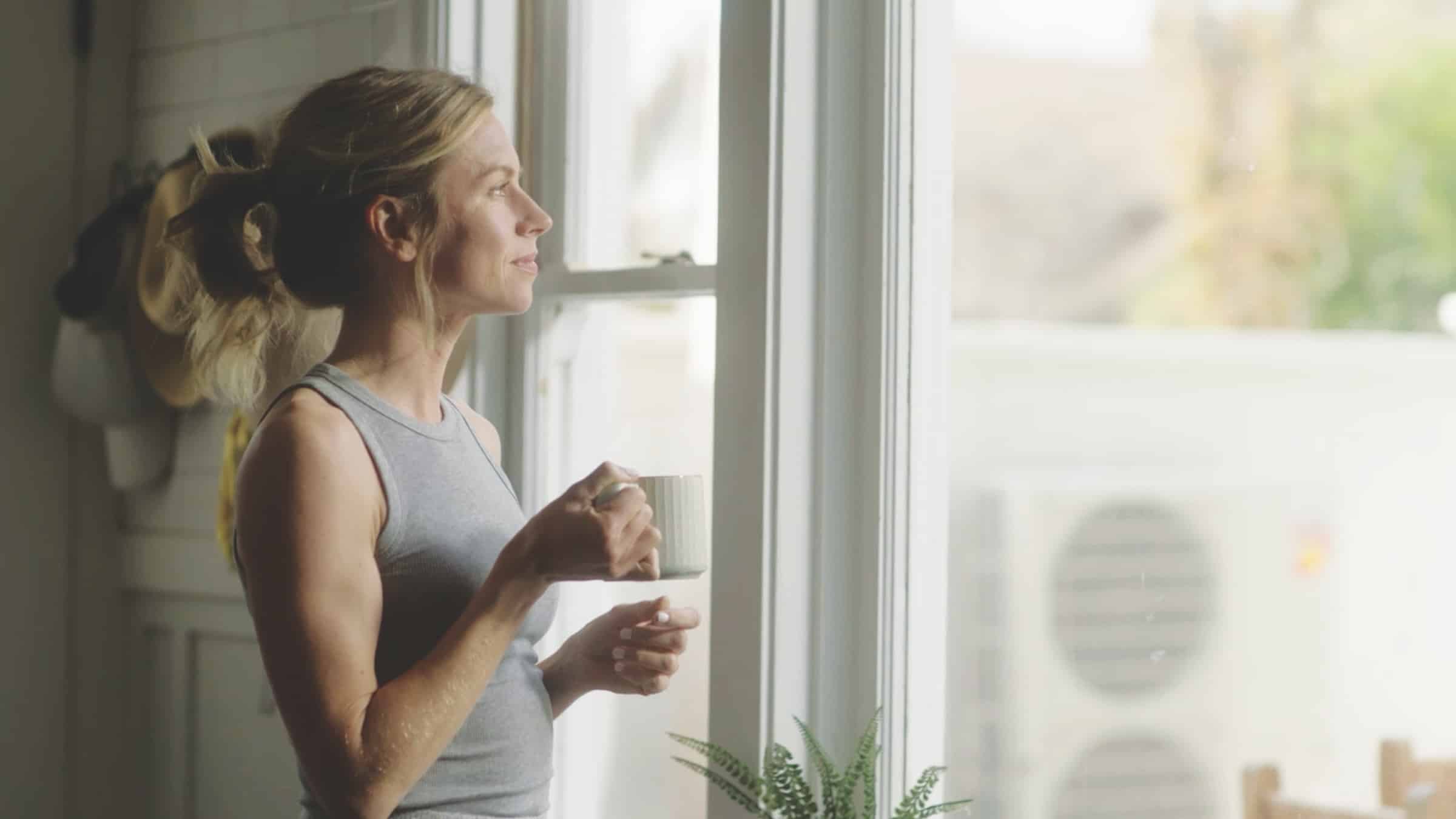 Comfortable Looking Woman In Kitchen With Heat Pump Outside Her Window